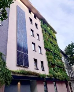 Clădire cu panouri pe fațadă și vegetație pe balcoane.