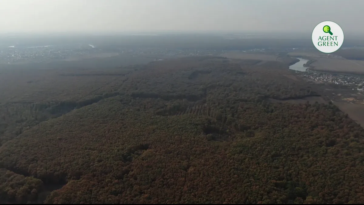 Vedere aeriană a unei păduri lângă clădiri și un lac, cu sigla Agent Green.
