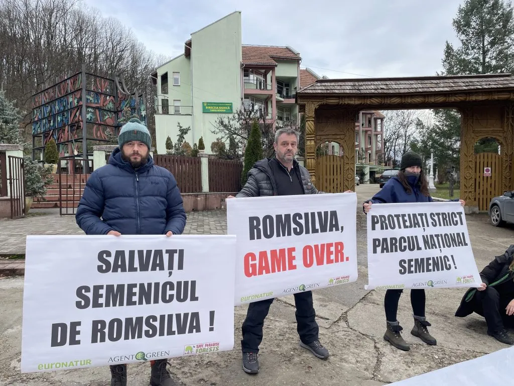 Trei persoane cu pancarte pentru protejarea Semenicului, în fața unei clădiri.