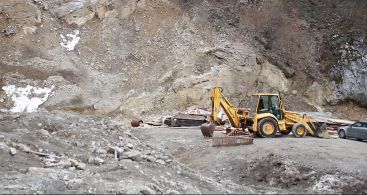 Utilaj galben pe un versant excavat și stâncos, lângă alte vehicule